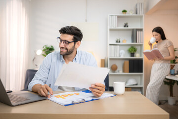Obraz premium Portrait of a young freelancer smiling while working online via laptop at home with his girlfriend