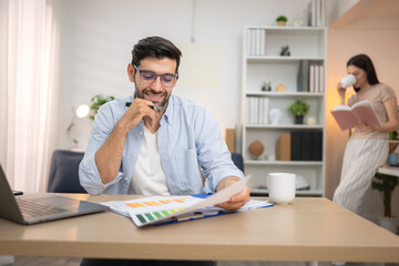 Portrait of a young freelancer smiling while working online via laptop at home with his girlfriend