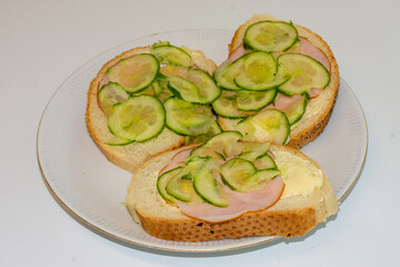 Simple yet tasty open-faced sandwiches feature creamy spread, layers of ham, and fresh cucumber slices arranged neatly. They sit invitingly on a white plate, ready to enjoy