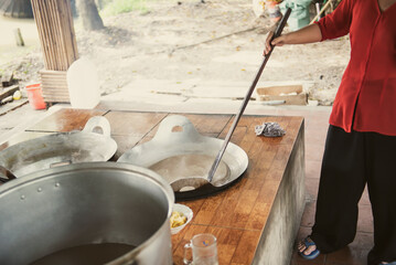 Southern Vietnamese lady in traditional dress stirring mixture of squeezed coconut milk, cream,...