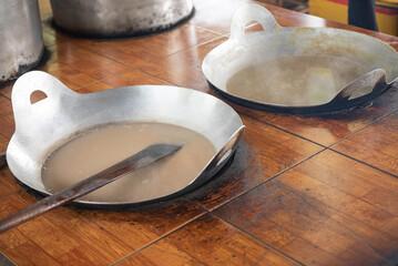 Mixture of squeezed coconut milk, cream, sugar and malt syrup in flat cast iron cooking pan at...