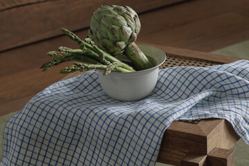 Fresh asparagus and artichoke in ceramic bowl on rattan stool with linen tea towel. Healthy...