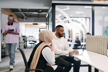 Obraz premium In a modern office setting, an African American businessman and his Muslim colleague, wearing a hijab, engage in collaborative discussions, tackling various business tasks and solving problems