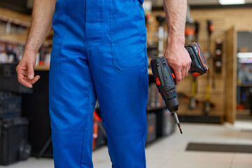 Crop portrait of repairman holding drill in hands over workshop interior