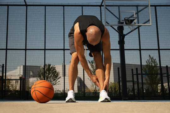 Basketball ankle injury or pain. Basketball player check legs after workout of sport stadium. Professional athlete or sportsman with accident. Man check pain in leg after sport workout.