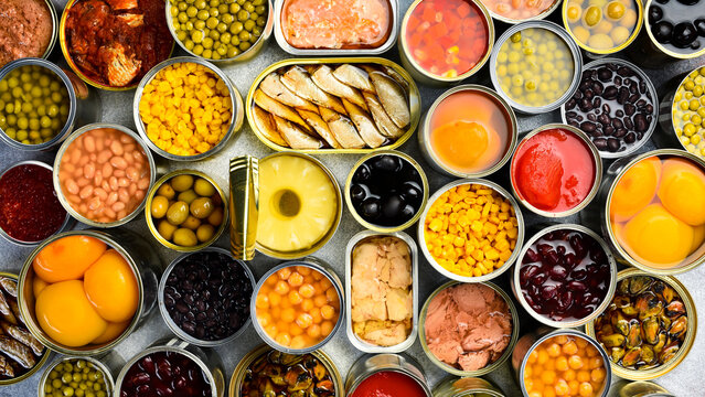 A large set of pickled and canned foods on the background. Metal cans with canned vegetables, beans, fish, seafood and fruit. Top view.