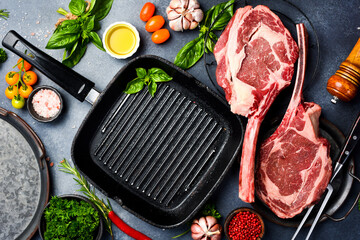 Raw Tomahawk Steak in a pan. Cooking Tomahawk steaks, spices, seasonings, butter and salt on a gray...