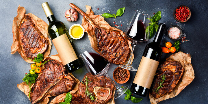 Background of wine and beef steaks. Premium red wine and Aged beef steaks on a gray stone background. Top view. Free space for text.