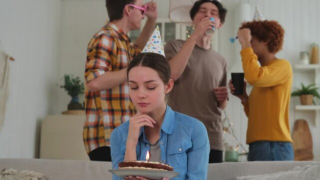 Sad lonely frustrated unhappy young woman looking at birthday cake with candle on birthday party. Girl sad disappointed thinking about life. Birthday party with friends. People celebrating birthday