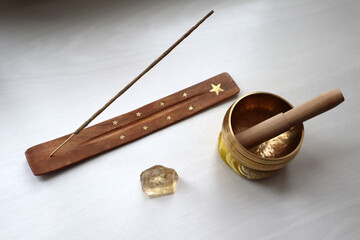 Indian incense, singing bowl and citrine crystal on white table.