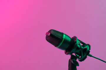Professional studio microphone with shock mount and cable, illuminated by green and pink light on a...