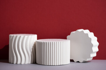 Geometric white podiums of different shapes on a gray table on a red wall. Premium scene for...