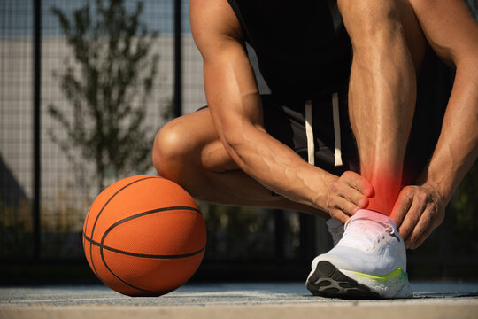 Basketball ankle injury or pain. Basketball player check legs after workout of sport stadium. Professional athlete or sportsman with accident. Man check pain in leg after sport workout.