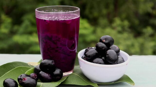 Jamun or Malabar Plum Juice in a Glass with Fruit in a Bowl with Leaves Isolated on Wooden  Background, Also Known as Black Plum, Syzygium Cumini or Jambolan