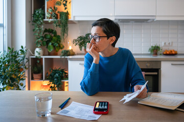 Concerned worried mature woman with bills and receipts, calculating budget and balancing expenses....