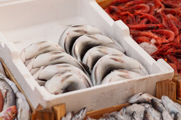 Whole fresh fish carefully folded and arranged in a white crate on ice at a seafood market, with...