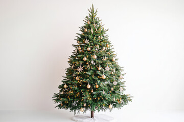 Fototapeta premium Elegant Christmas tree with golden ornaments and warm fairy lights against a white background