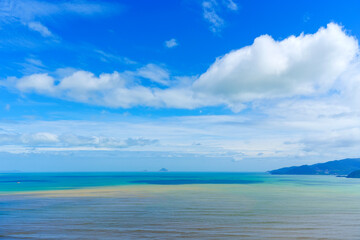 Bright blue skies highlight the turquoise and brown hues of the ocean, with distant mountains framing the shoreline. The scene suggests a calm yet dynamic atmosphere, perfect for exploration