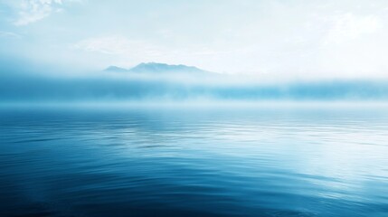 Fototapeta premium Tranquil misty lake with distant mountains under clear sky