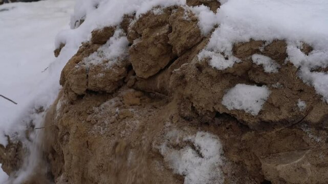 A shovel breaks a pile of sand and clay in the snow in winter