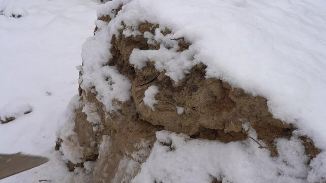 A shovel breaks a frozen pile of sand with clay in winter in the snow slowmo