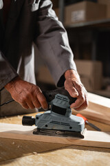 Close-up of carpenters hands grinding wood with sander machine in carpentry diy workshop. Electric sander