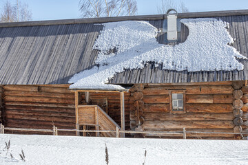 An old wooden log house built in the 19th century. Village house in Khokhlovka. Winter landscape in the village. There is snow on the wooden roof of the old house. Warming after winter frosts. © Eduard Belkin