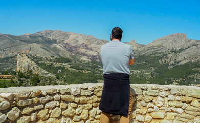 Man observing a mountainous landscape from a stone wall