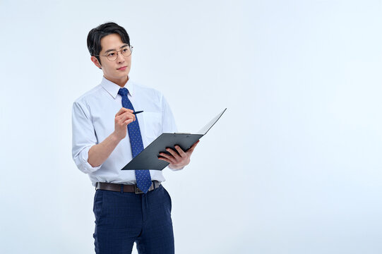 A young male teacher wearing a suit and glasses is holding a notebook in a classroom and conducting a lesson in various poses and facial expressions.