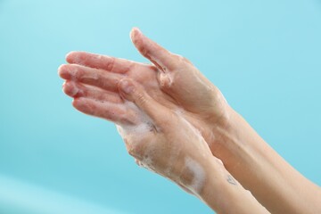 Fototapeta premium Woman washing hands with foaming soap on light blue background, closeup. Hygiene