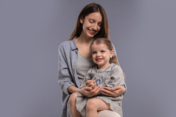 Happy mother with her cute little daughter on grey background