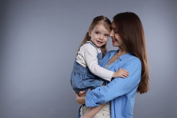 Happy mother with her cute little daughter on grey background, space for text