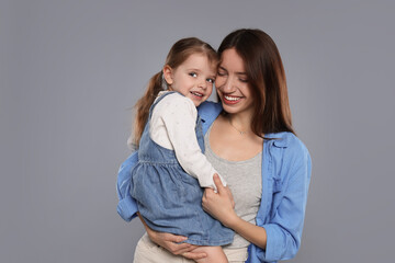 Happy mother with her cute little daughter on grey background