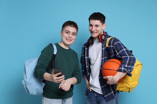Students with backpacks, smartphone and basketball ball on light blue background