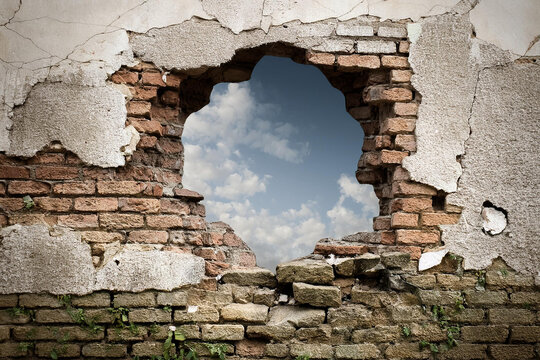 Hope and freedom concept, Brick wall with hole revealing lush greenery, natural light. Royalty high-quality free best stock of broken brick wall revealing a serene landscape with mountains, trees