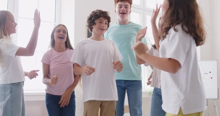 Happy smiling school students group having fun jumping in classroom together. Schoolchildren giving high five each other and hugging. Education and back to school concept. 4k video. Slow motion video