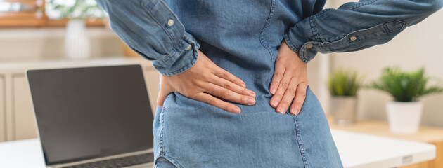 Close-up woman massaging her lower back has back pain because of sitting posture during work in...