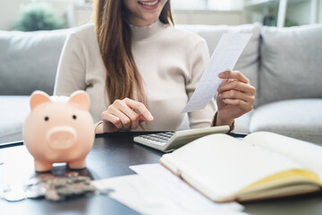 Young woman saving money monthly expenses putting coin in to piggy bank on the table.