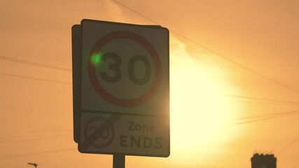 Speed limit sign against bright sunlight. Traffic sign outline in early sunlight. Maximum velocity thirty miles board appearing as dark contour in golden morning glow