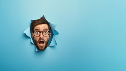Portrait of a surprised businessman with glasses and beard peeking through a ripped hole in blue paper