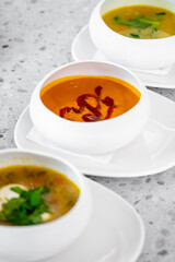 Three bowls of soup featuring vibrant colors and garnishes, served on elegant white plates. The dishes showcase a variety of textures and ingredients, perfect for a culinary showcase.
