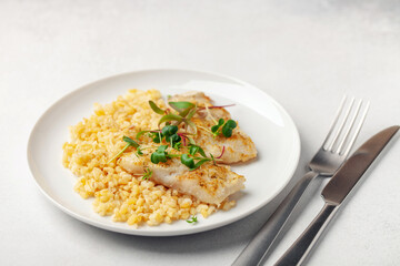 Baked fish hake or pollock and garnish bulgur and microgreens in a plate on the table. Healthy food