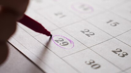 A person with a violet felt-tip pen traces the dates in the calendar. planning and marking important events and plans.