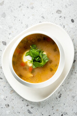 A bowl of delicious soup garnished with fresh cilantro on a textured surface, featuring vibrant vegetables and a creamy swirl, perfect for showcasing comforting culinary delights