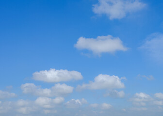 A blue sky background with white cumulus clouds. The clouds are fluffy and bright against the blue sky.