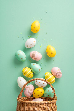 Naklejki Festive vertical arrangement of colorful patterned Easter eggs spilling from a woven basket on a pastel green background, symbolizing Easter celebrations and springtime joy