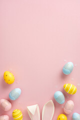 Decorative Easter eggs and bunny ears placed artistically on a pink minimalistic background