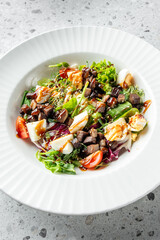 A fresh salad featuring mixed greens, cherry tomatoes, chopped eggs, and savory toppings drizzled with a light dressing, served in an elegant white plate.