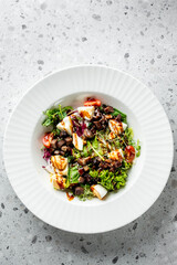 A fresh salad featuring mixed greens, cherry tomatoes, chopped eggs, and savory toppings drizzled with a light dressing, served in an elegant white plate.