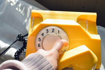 A person dials a number on a vibrant yellow vintage rotary phone with a classic design.